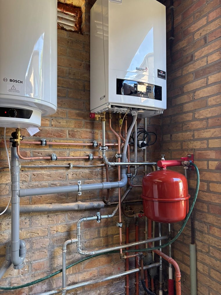 Cv-ketel en boiler met netjes afgewerkt leidingwerk op een gemetselde muur