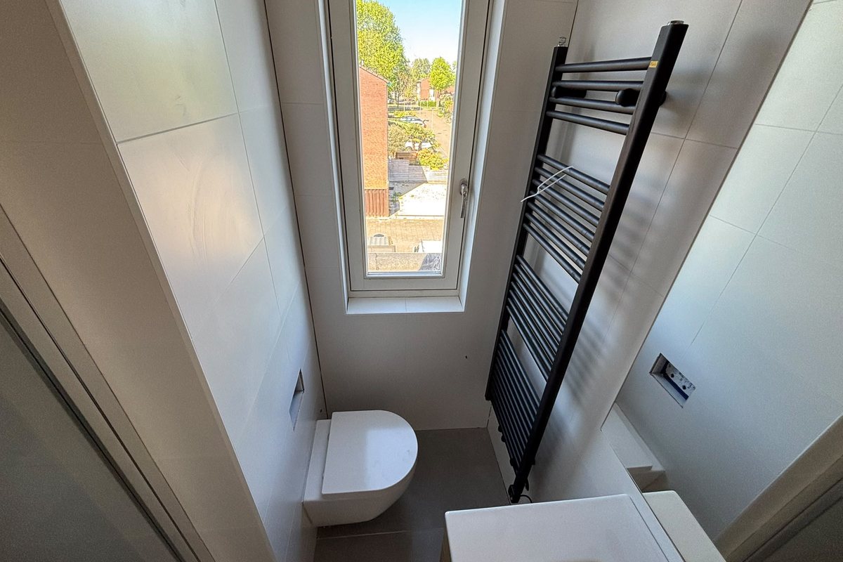 Gerenoveerde badkamer met hangend toilet, designradiator en groot tegelwerk